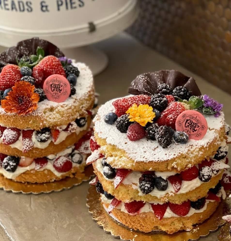 Two mini layer cakes decorated with strawberries, blueberries, blackberries, cream, and edible flowers