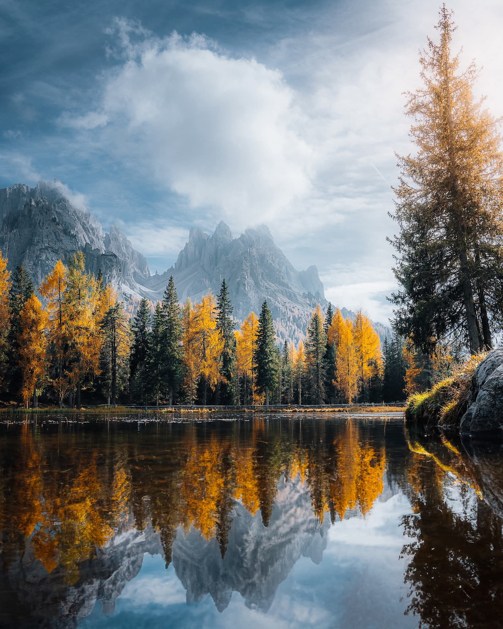 Alpine lake reflecting golden autumn trees and rocky mountain peaks under dramatic clouds