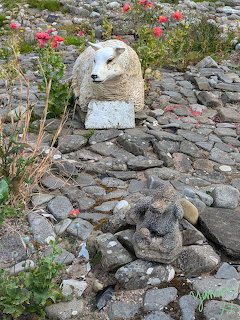 Two stone sheep sculptures on a cobblestone path with red flowers in the background
