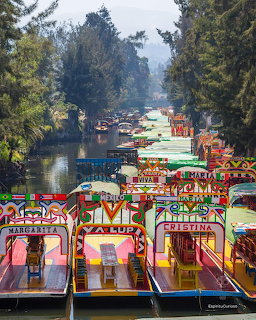 Colorful wooden trajinera boats with painted names docked along a canal in Xochimilco, Mexico