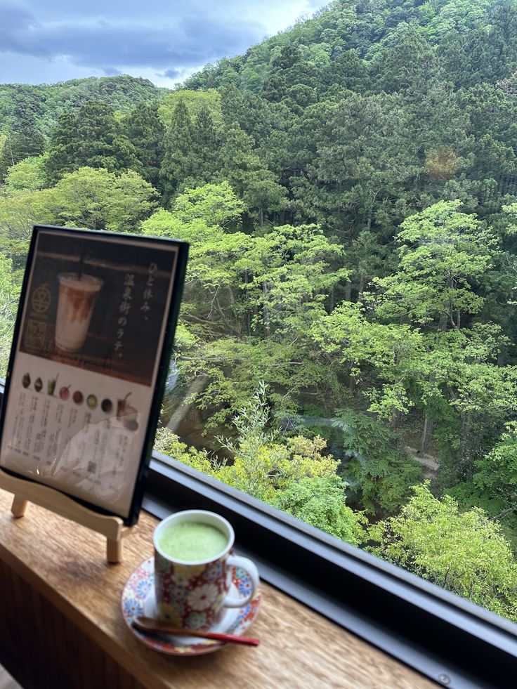 Matcha latte cup on a cafe windowsill with a dense green forest view in the background