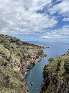Rocky sea cliffs and a narrow blue inlet beneath a partly cloudy sky