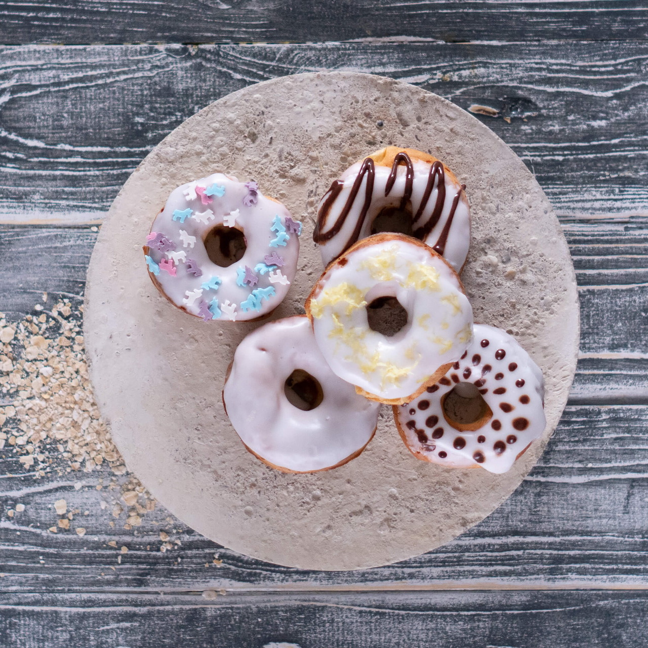 Five glazed donuts with various toppings on a round plate viewed from above