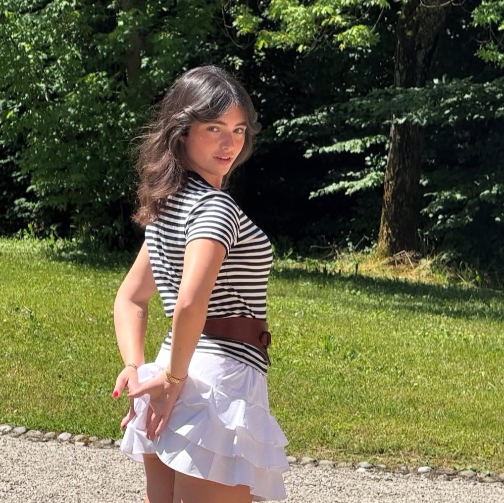 Woman in black and white striped shirt and white skirt standing outdoors near trees