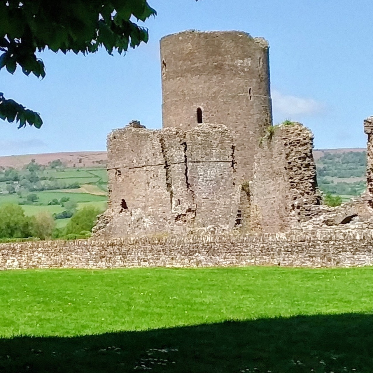 Stone ruins of Tretower Castle with round tower, grass lawn, and green hills under blue sky