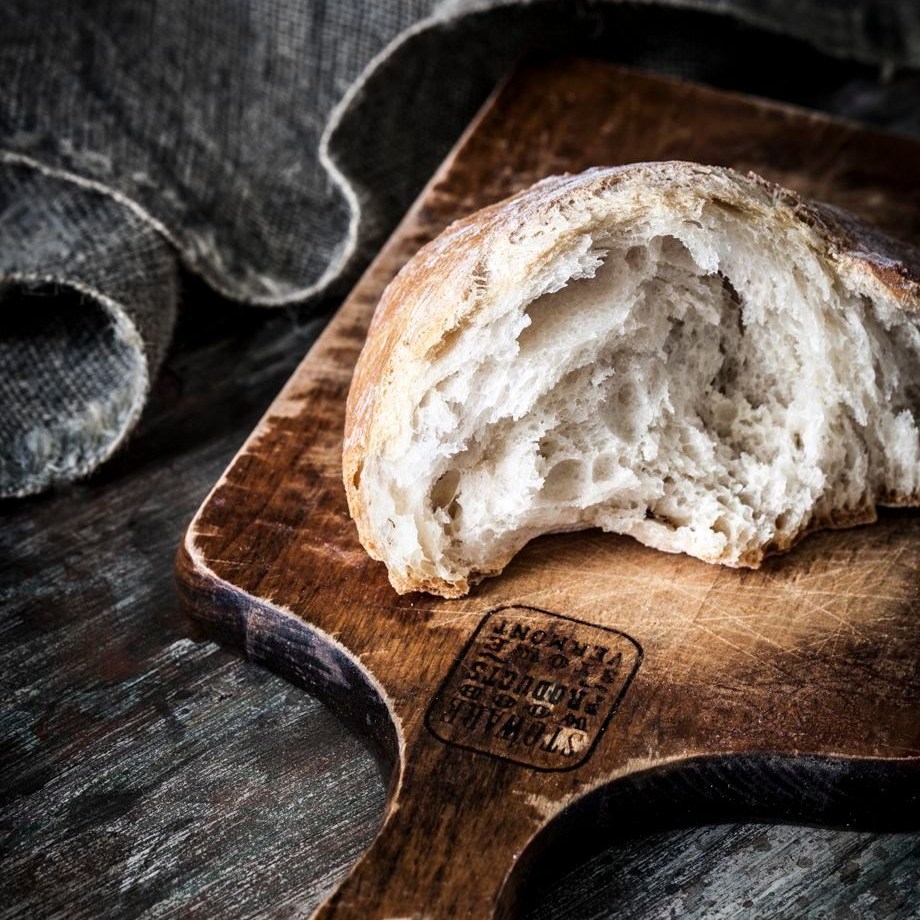 Sliced rustic bread loaf on wooden board with dark cloth