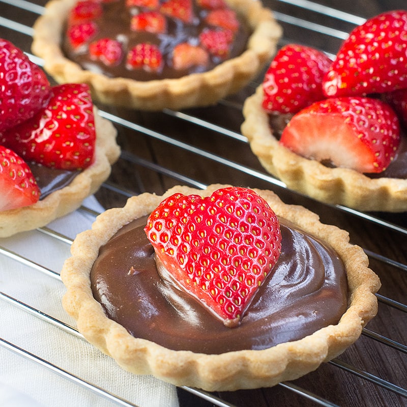 Chocolate tartlets topped with strawberries on a metal cooling rack