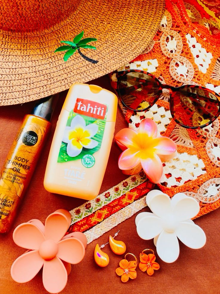 Flat lay of summer beach items: straw hat, Tahiti body wash, sunglasses, sunscreen, and tropical flowers