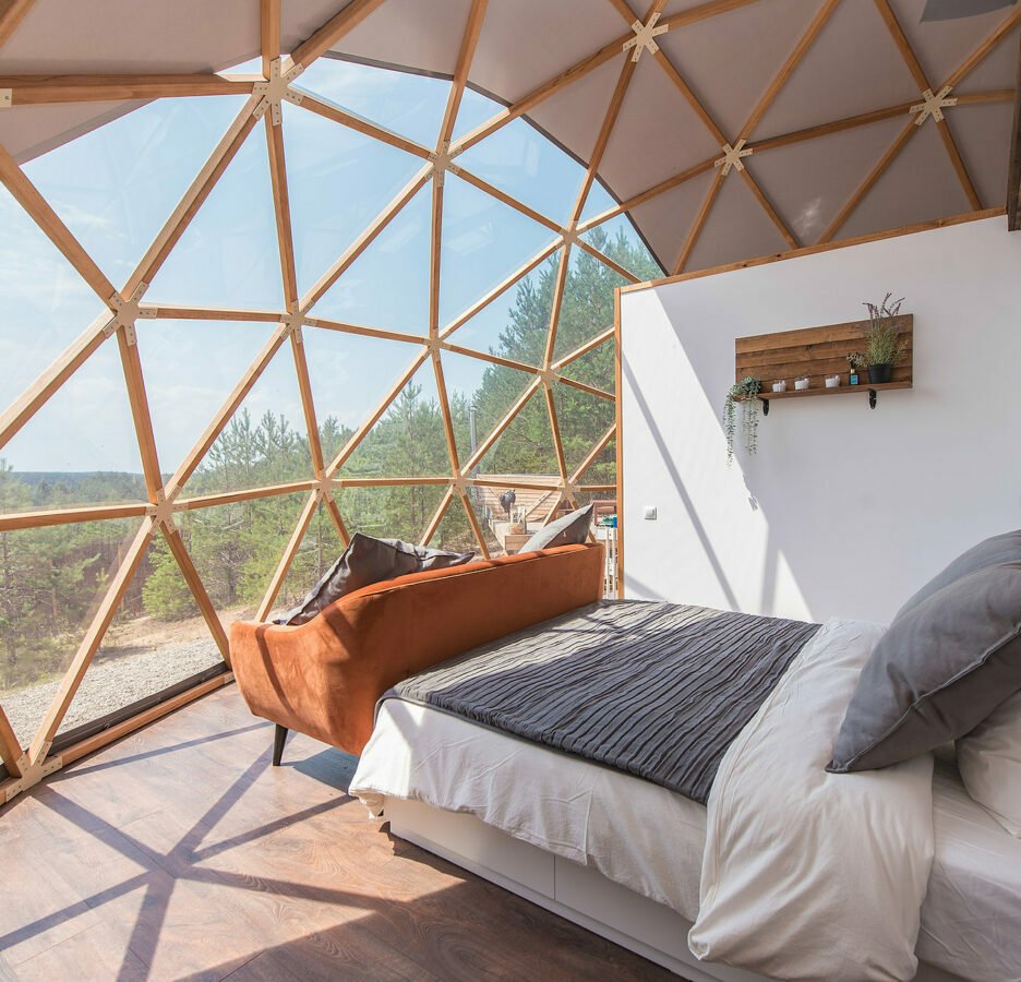 Bright bedroom inside a geodesic dome with bed, sofa, and large triangular windows