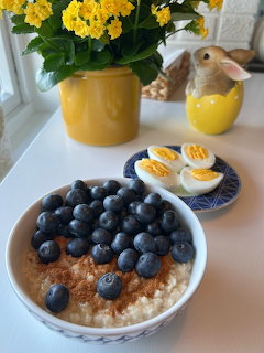 Bowl of blueberry oatmeal with sliced boiled eggs and yellow flowers on a table