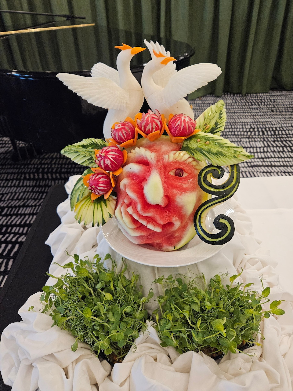 Carved watermelon centerpiece with flower design, white swans, and green leaves on a pedestal