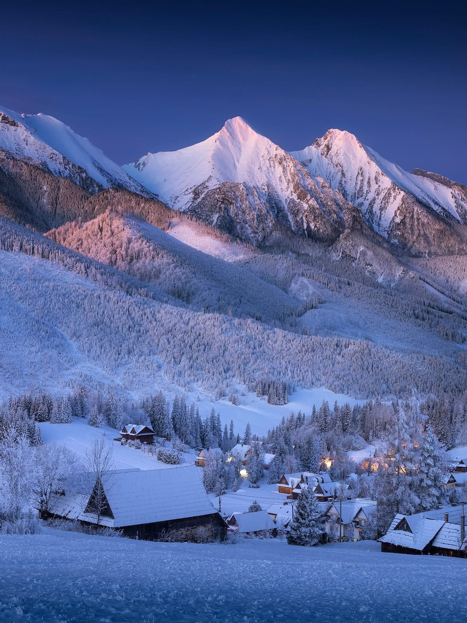Snowy mountain village with illuminated peaks at twilight in winter alpine landscape