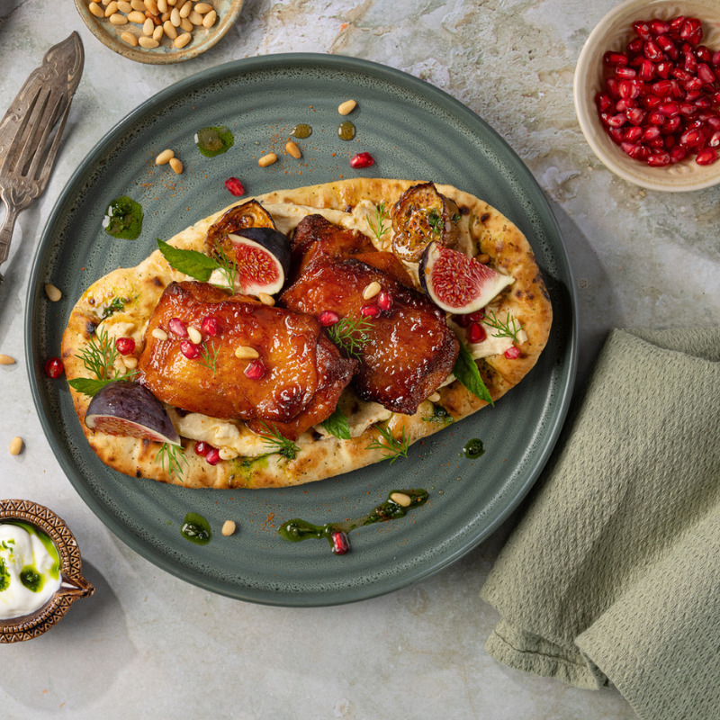 Honey-glazed chicken thighs on flatbread with figs and pomegranate on a blue ceramic plate