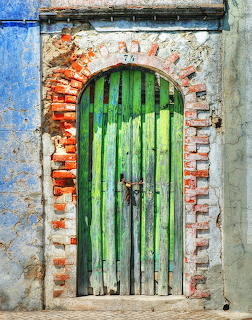 Weathered green wooden door in brick archway with peeling blue painted wall