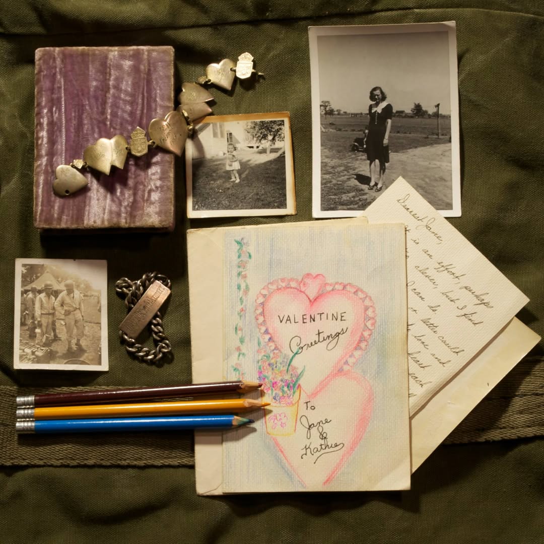 Vintage photos, letters, Valentine card, pencils, and a small gift box arranged on green fabric