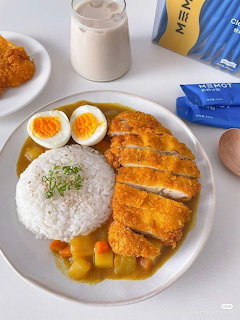 Plate of chicken katsu curry with rice and soft-boiled eggs, fried chicken and drink in background
