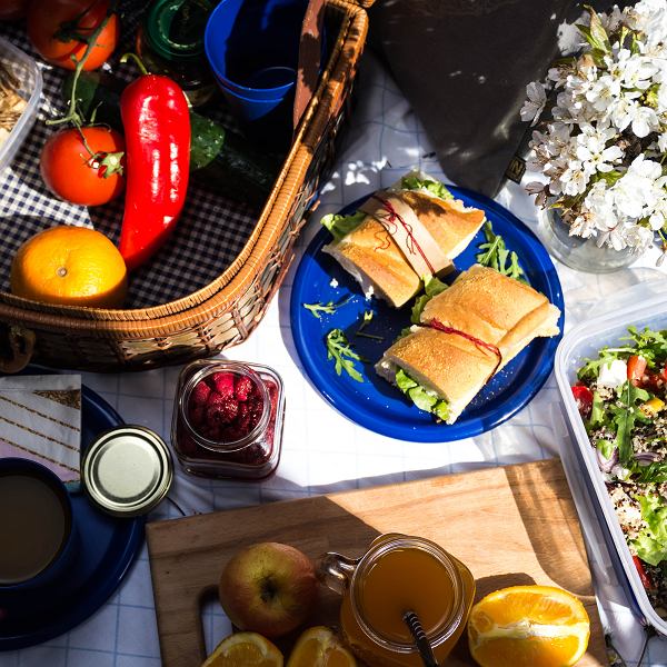 Overhead view of picnic spread with sandwiches, vegetables, salads and drinks on wooden table