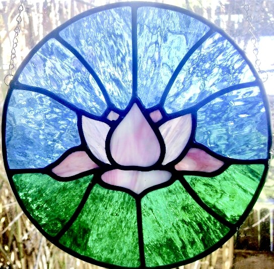 Circular stained glass panel with pink lotus, blue sky, and green grass