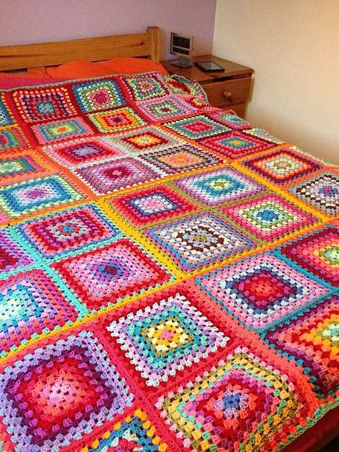 Colorful crochet granny square blanket on wooden bed with nightstand
