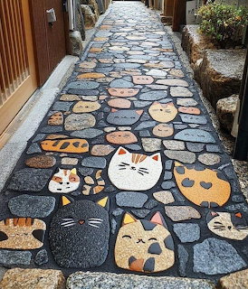 Stone path with mosaic cat faces and paw prints embedded in dark cobblestones