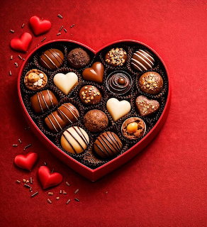 Heart-shaped box of assorted chocolates on red background with small decorative hearts