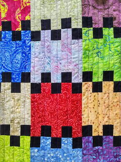Colorful patchwork quilt with bright fabric squares and black checkerboard pattern borders