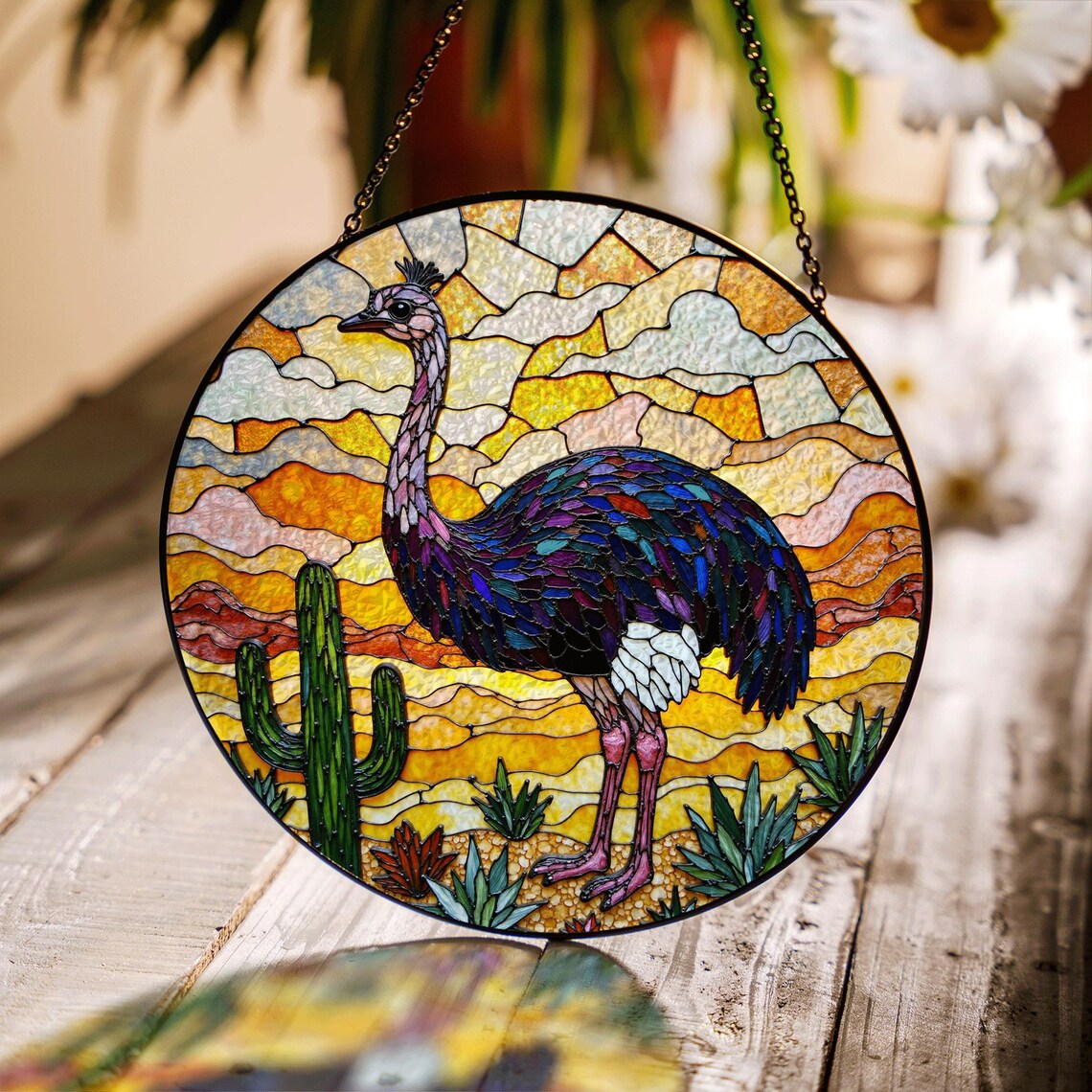 Round ostrich suncatcher with stained glass-style desert scene hanging over a wooden table