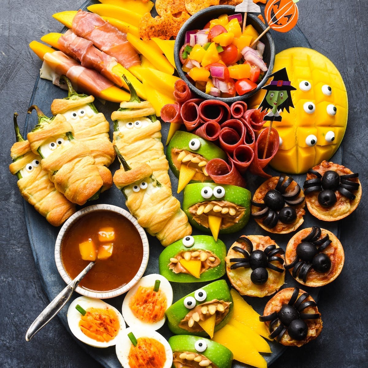 Halloween party food platter with mummy wraps, cookies, candy corn, and spooky decorated snacks