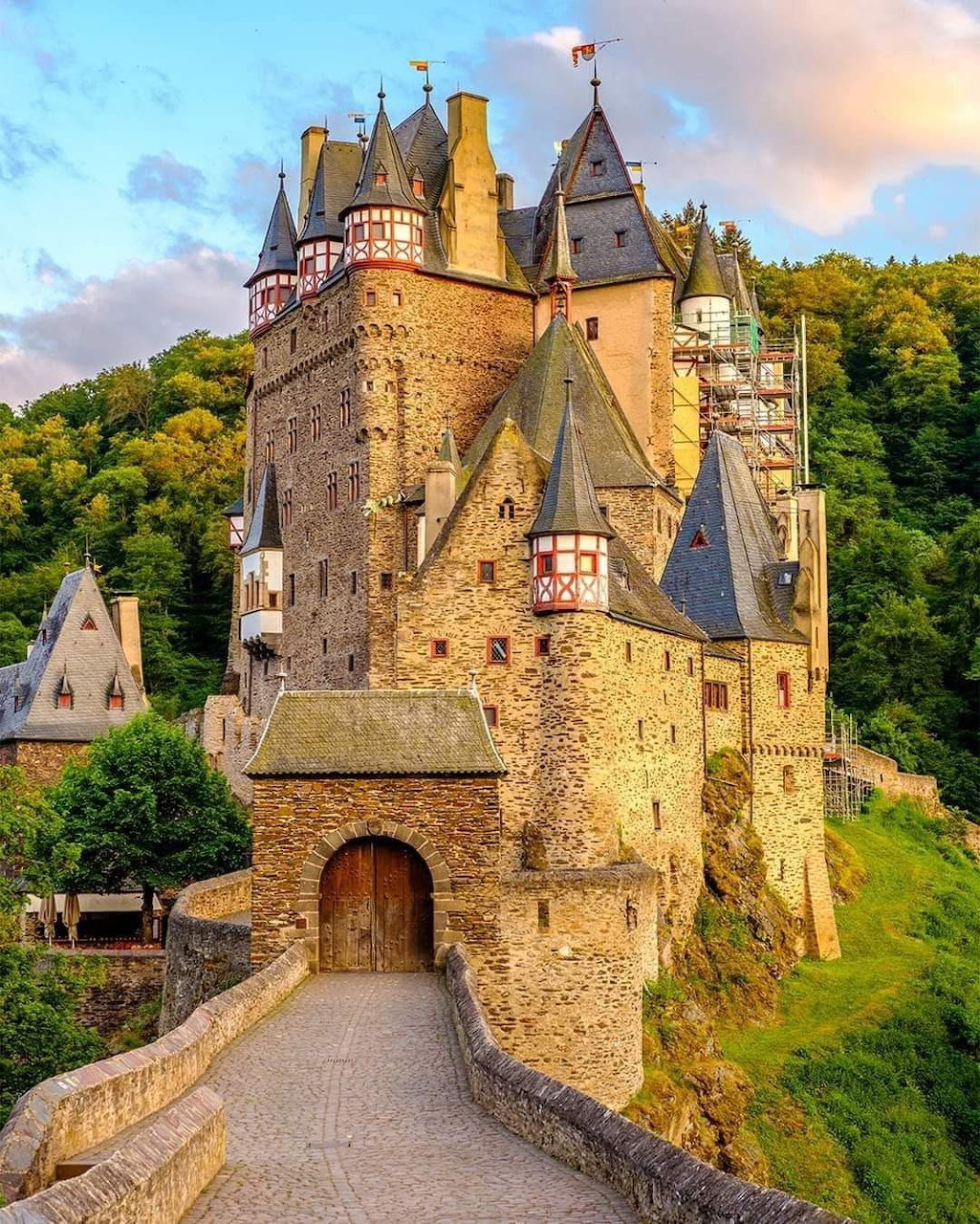 Medieval castle with multiple towers and turrets surrounded by green forest under sunset sky