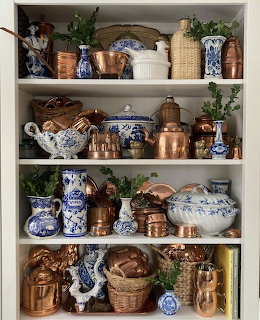 White shelves filled with copper cookware and blue and white china with green ivy trailing between items