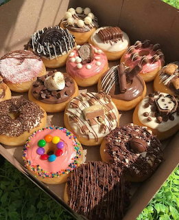 Open box filled with assorted decorated donuts with various toppings on grass