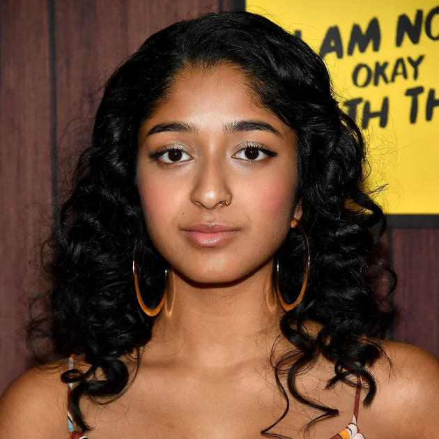 Young woman with curly black hair and gold hoop earrings smiling at an event