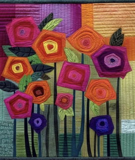 Colorful quilted textile art with abstract circular flowers in pink, orange, purple against striped multicolor background