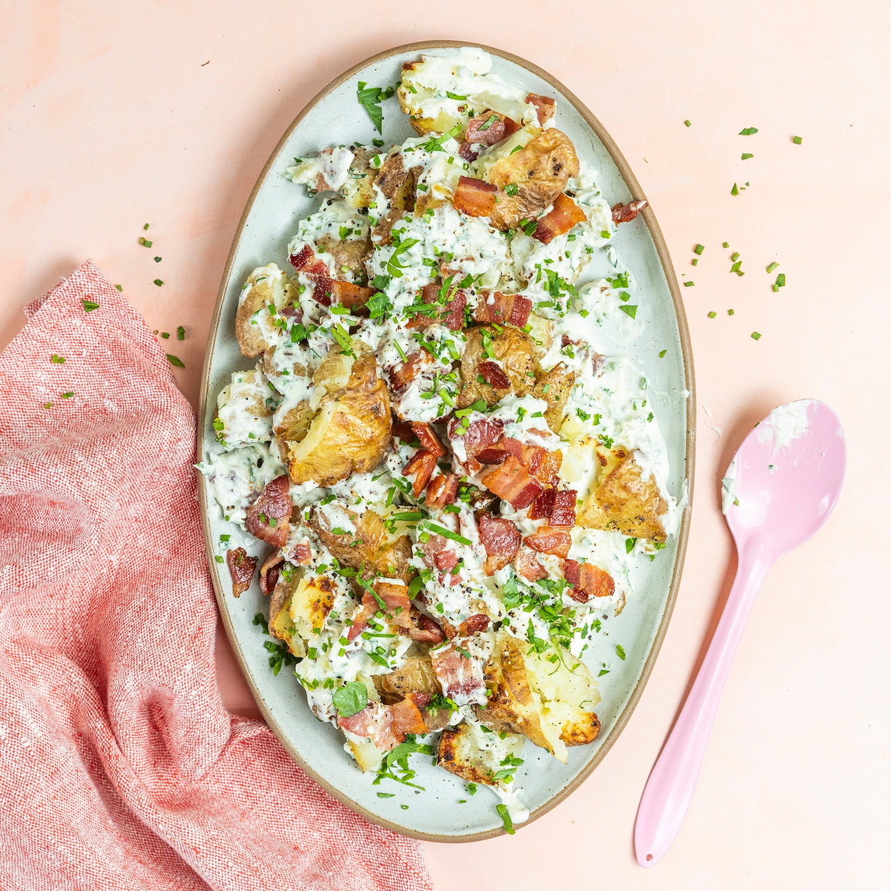 Oval plate of ham and eggs with herbs and cheese beside a pink spoon and cloth