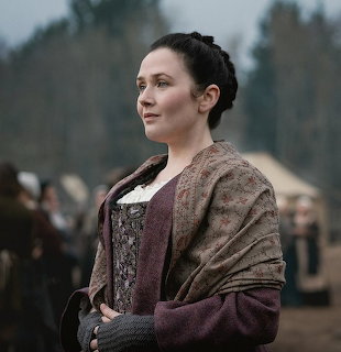 Woman in historical dress standing outdoors with a blurred crowd behind her
