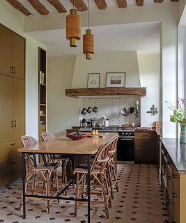 Rustic kitchen interior with wooden table, woven chairs, exposed beams, and patterned tile floor