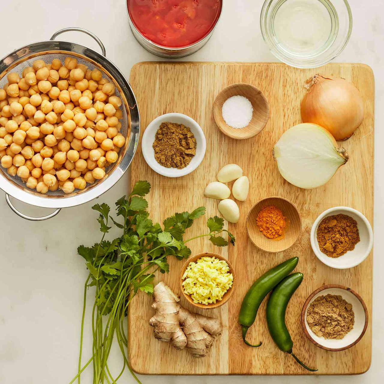 Overhead view of chickpea curry ingredients arranged on wooden cutting board with spices and fresh vegetables