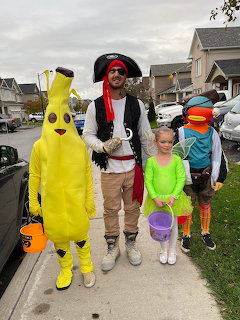 Three people in Halloween costumes standing on suburban sidewalk with trick-or-treat baskets