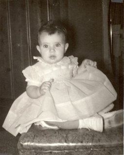 Vintage black-and-white portrait of a baby girl in a frilly dress sitting on a cushioned stool