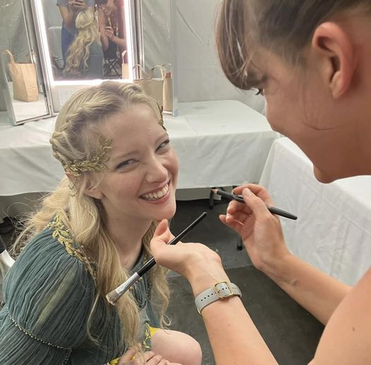 Smiling blonde woman having makeup applied by another woman indoors