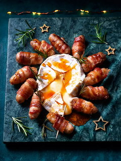 Sausages arranged in a circle around a fried egg on a dark slate board with rosemary and star decorations