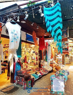 Vibrant souvenir shop entrance with blue striped fabrics hanging overhead and colorful Turkish goods on display