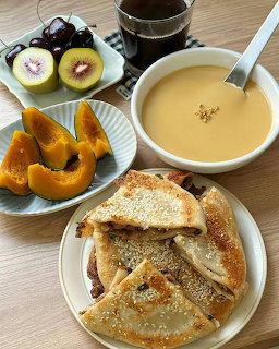 Tabletop meal with toasted sandwiches, creamy soup, coffee, pumpkin, kiwi, and grapes