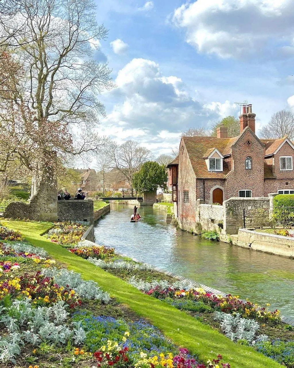 Stone cottage beside river with spring flower beds and bridge in Canterbury