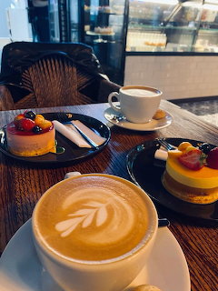 Latte with foam art next to assorted fancy desserts on a table