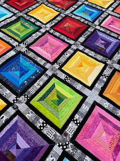 Colorful quilt with concentric square blocks in rainbow hues separated by black and white floral borders