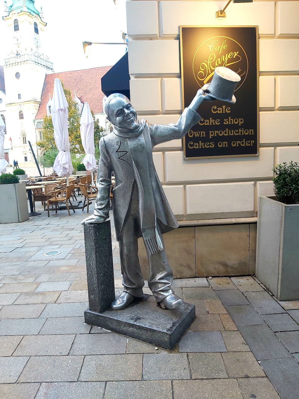 Bronze statue of man in suit and hat leaning on lamppost in town square
