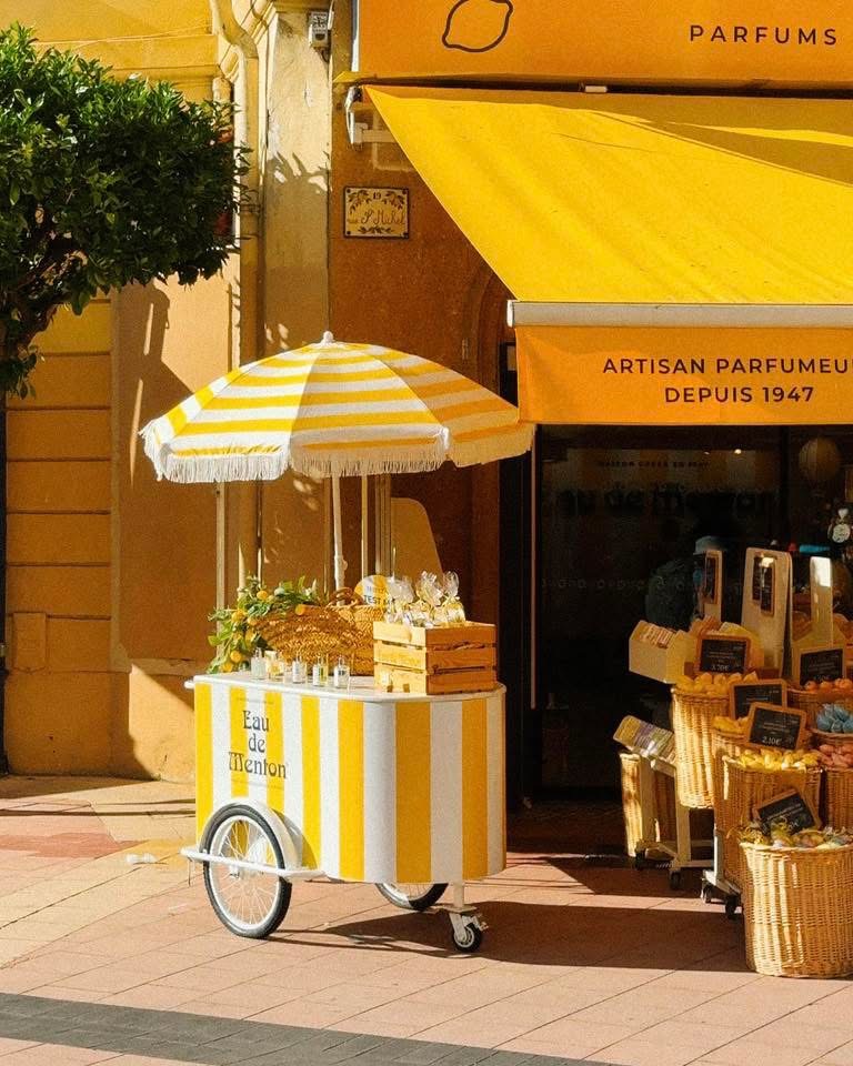 Yellow and white striped ice cream cart on a sunny street in Menton, France, in front of a perfume boutique