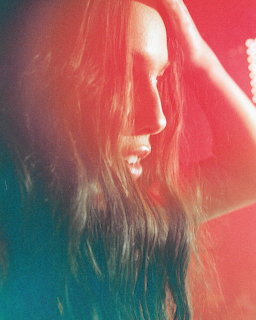 Side profile of woman with long dark hair against red-teal gradient background, hand touching head