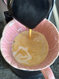 Coffee pouring from a coffee maker into a pink ceramic mug